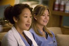 two women in scrubs are sitting on a couch and one is looking at the camera