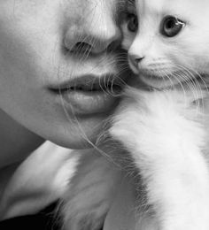 a black and white photo of a woman holding a kitten in her arms, looking at the camera