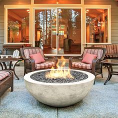 an outdoor fire pit sitting on top of a patio next to chairs and tables with cushions