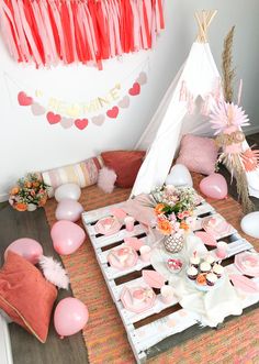 a pink and white birthday party with balloons, cake, cupcakes and teepee