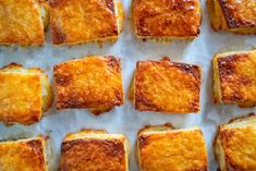 several square pieces of bread sitting on top of a piece of parchment paper with melted cheese