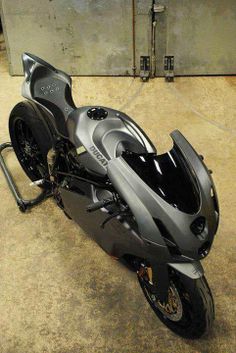 a silver motorcycle parked in a garage next to a metal object on the ground with it's front wheel still attached