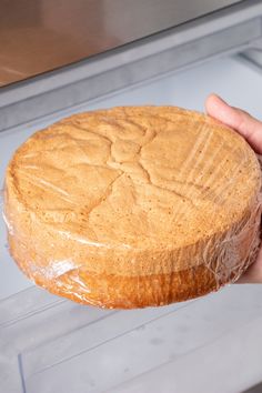 a person holding a round cake in front of a display case with frosting on it