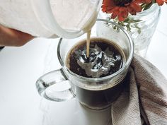 someone pours coffee into a mug with flowers in the background