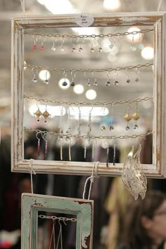 an old window frame with earrings hanging from it's sides in front of a store display