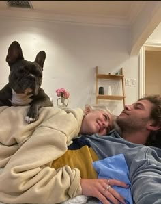 a man laying in bed next to a woman with a dog on his back and she has her arm around him