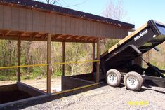 a dump truck is parked in front of a covered area with trees and bushes behind it