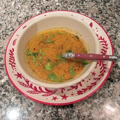 a red and white bowl filled with soup on top of a table next to a spoon