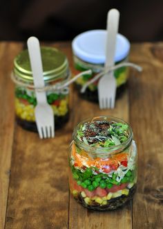 three mason jars filled with food and plastic forks sitting on top of a wooden table