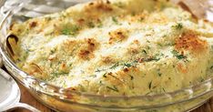 a casserole dish with cheese and herbs in it on a wooden table next to two spoons