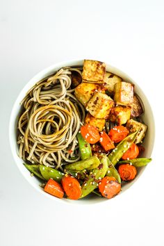 a white bowl filled with noodles, tofu and veggies on top of it