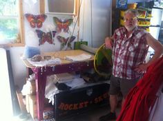 a man standing in front of a desk with lots of clutter on it and butterfly decorations behind him