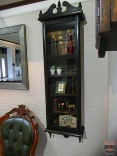 a chair sitting next to a shelf with pictures and other items on it in front of a mirror