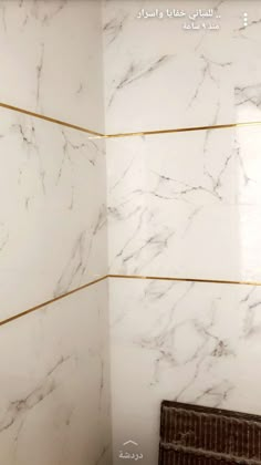 the corner of a bathroom with white marble walls and gold lines on the shower wall