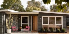 a small gray house with two pink chairs and a cactus in the front garden area