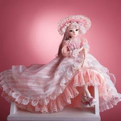 a doll sitting on top of a white table wearing a pink dress and matching shoes