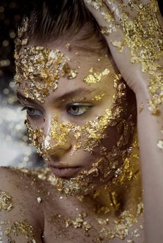 a woman with gold glitter on her face and hands behind her head, covering her eyes