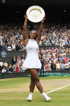 a woman holding up a tennis racquet on top of a tennis court in front of a crowd