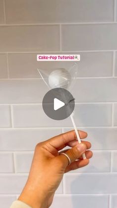 a person holding a lollipop in front of a white brick wall with the word cake pop on it