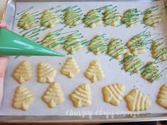 someone is decorating cookies with icing and green sprinkles on a baking sheet