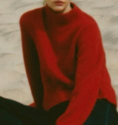 a woman sitting on the ground wearing a red sweater