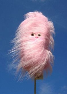 a pink troll doll on top of a pole with blue sky in the back ground