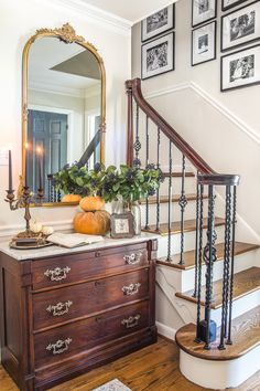 a wooden dresser sitting in front of a stair case next to a mirror and pictures on the wall