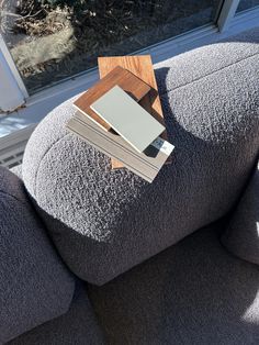 a stack of books sitting on top of a gray couch next to a window sill