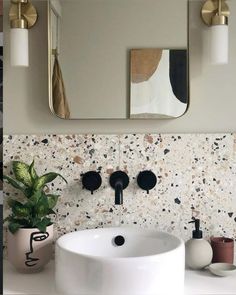 a white sink sitting under a bathroom mirror next to a potted plant on top of a counter