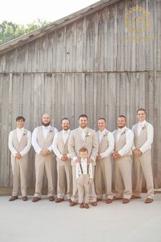 a group of men standing next to each other in front of a wooden barn wall