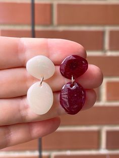 two white and red earrings are being held in front of a brick wall by someone's hand