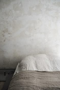 an unmade bed sitting next to a white wall