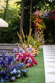 a row of benches sitting on top of a lush green field next to flowers and trees