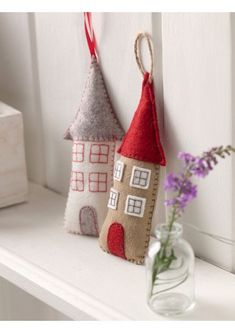 two small houses are hanging on the wall next to a vase with flowers in it