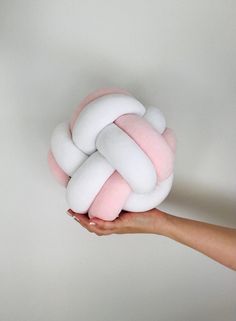 a hand holding a pink and white knot pillow