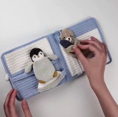 someone is holding a crocheted stuffed animal in front of an open book with two penguins on it