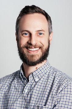 a man with a beard and blue eyes smiling at the camera while wearing a checkered shirt