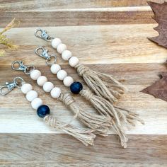 three tassels with beads and charms on a wooden table next to an autumn leaf