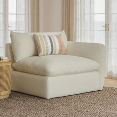 a white chair sitting in front of a window next to a table with a lamp on it