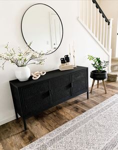 a black and white sideboard with plants on it in front of a mirror, stairs and potted plant