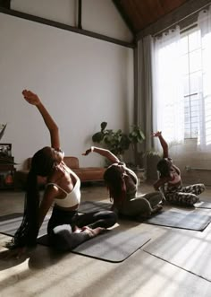 three women doing yoga on mats in a room with sunlight streaming through the window and potted plants