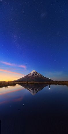 the night sky is reflected in the still waters of a lake with a snow - capped mountain in the distance