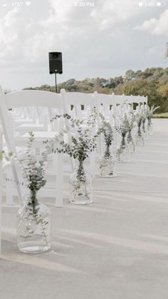 rows of white chairs with flowers in vases on the aisle for an outdoor ceremony