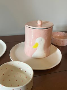 a table topped with plates and bowls covered in pink painted pottery next to a canister