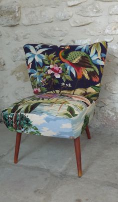 an upholstered chair with floral fabric and wooden legs, against a stone wall