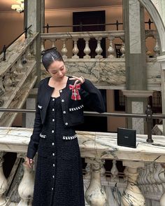 a woman standing in front of a staircase wearing a black dress and cardigan jacket