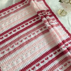 a pink and white crocheted blanket sitting on top of a bed next to flowers