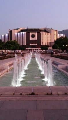 a large fountain in front of a building with many lights on it's sides