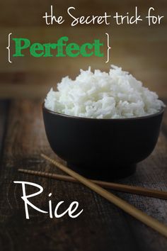 white rice in a black bowl with chopsticks on the side and wooden table