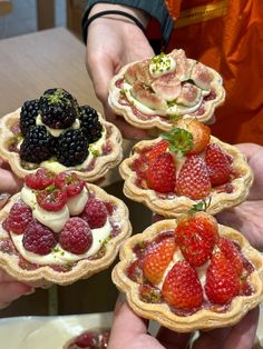 four small pies with fruit on them being held by two hands